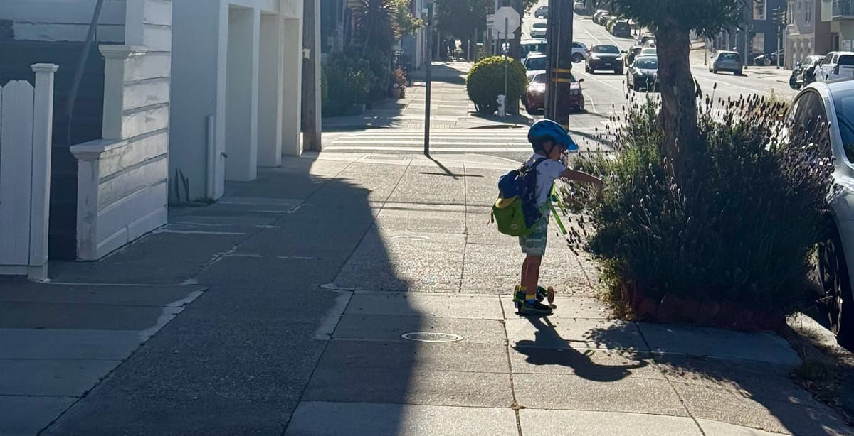 A young boy on a scooter reaching into a lavender bush